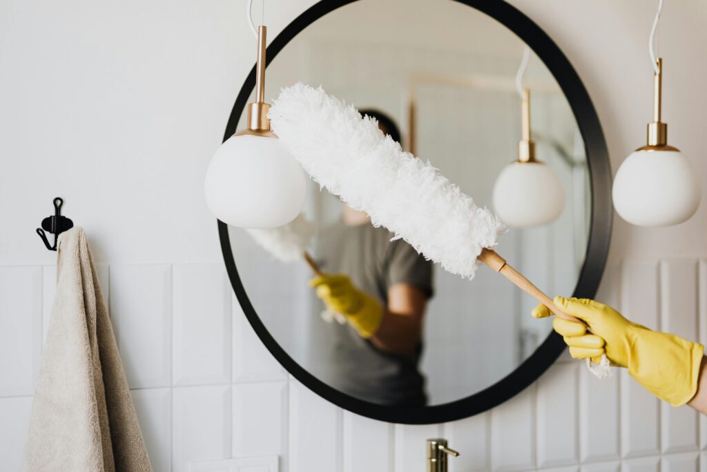 A gloved hand dusting a bathroom light fixture